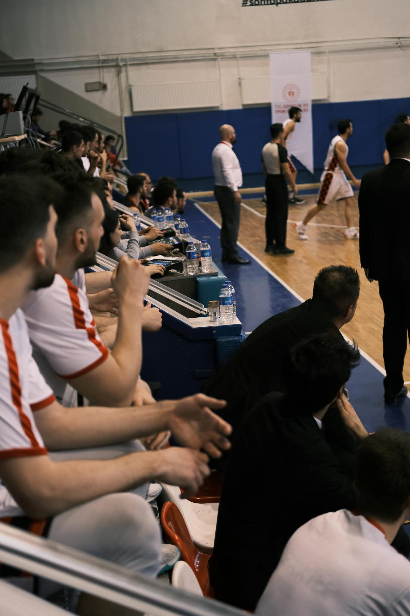 Players and spectators engage during an intense basketball game in a Turkish gym.